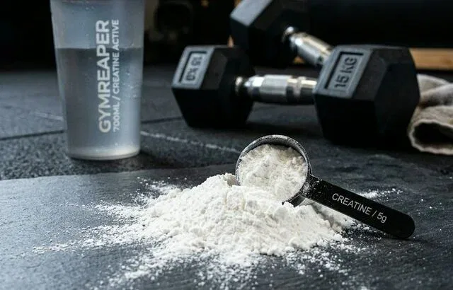 Creatine monohydrate powder with measuring scoop and gym equipment