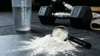 Creatine monohydrate powder with measuring scoop and gym equipment